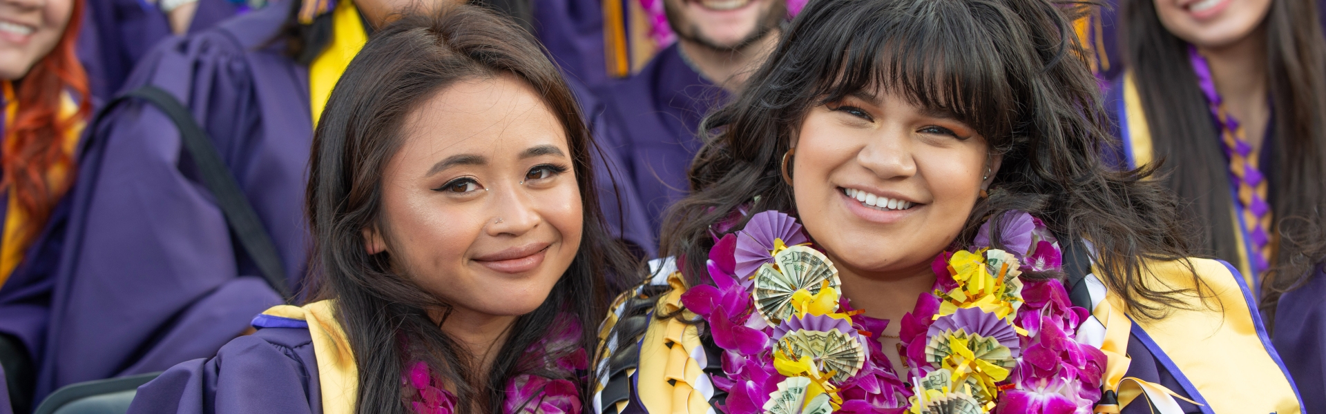 Two women dressed in regalia pose for a photo