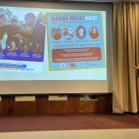 Carolyn Sideco addresses an adience while a PPT is projected on a screen behind her